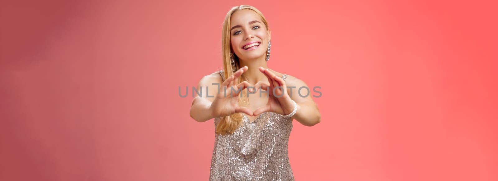 Girl confess she loves you. Portrait charming tender feminine young glamour blond woman in silver stylish glittering dress extend arms camera show heart sign smiling broadly, adore girlfriend.