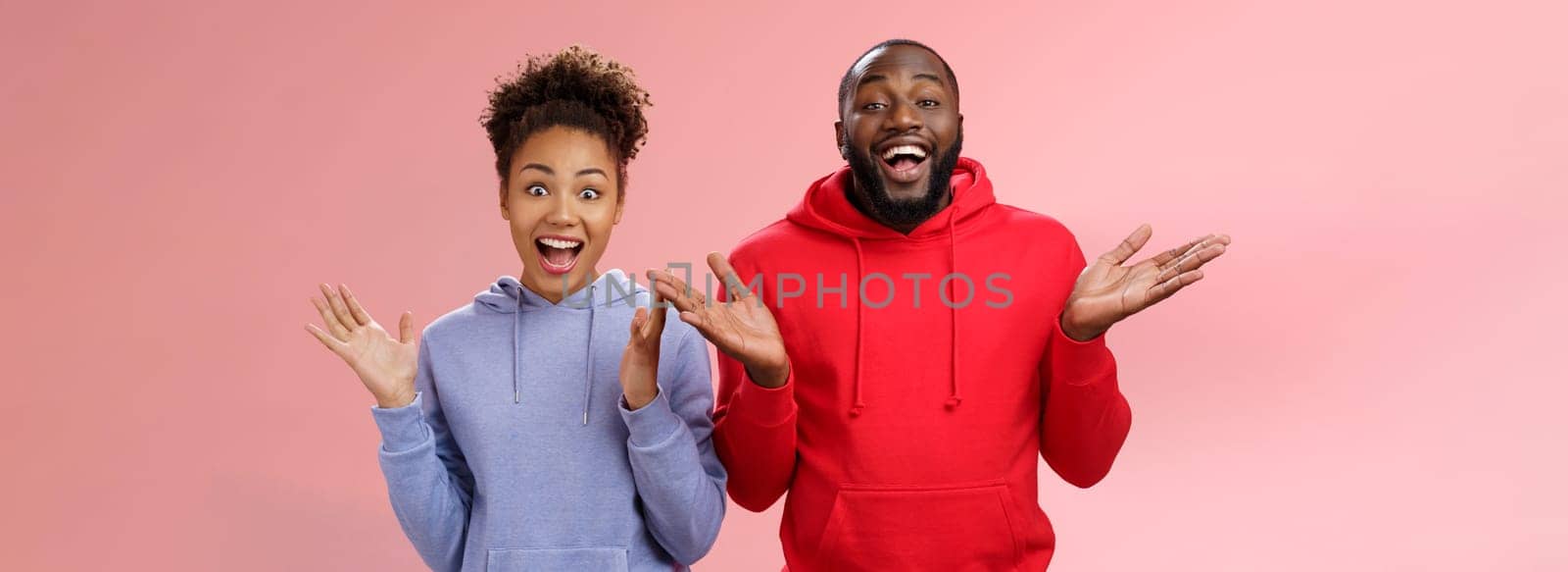 Guys receive nice surprise. Two attractive carefree surprised happy african man woman clapping hands joyfully greeting welcoming guests inviting people joing party standing friendly pink background by Benzoix