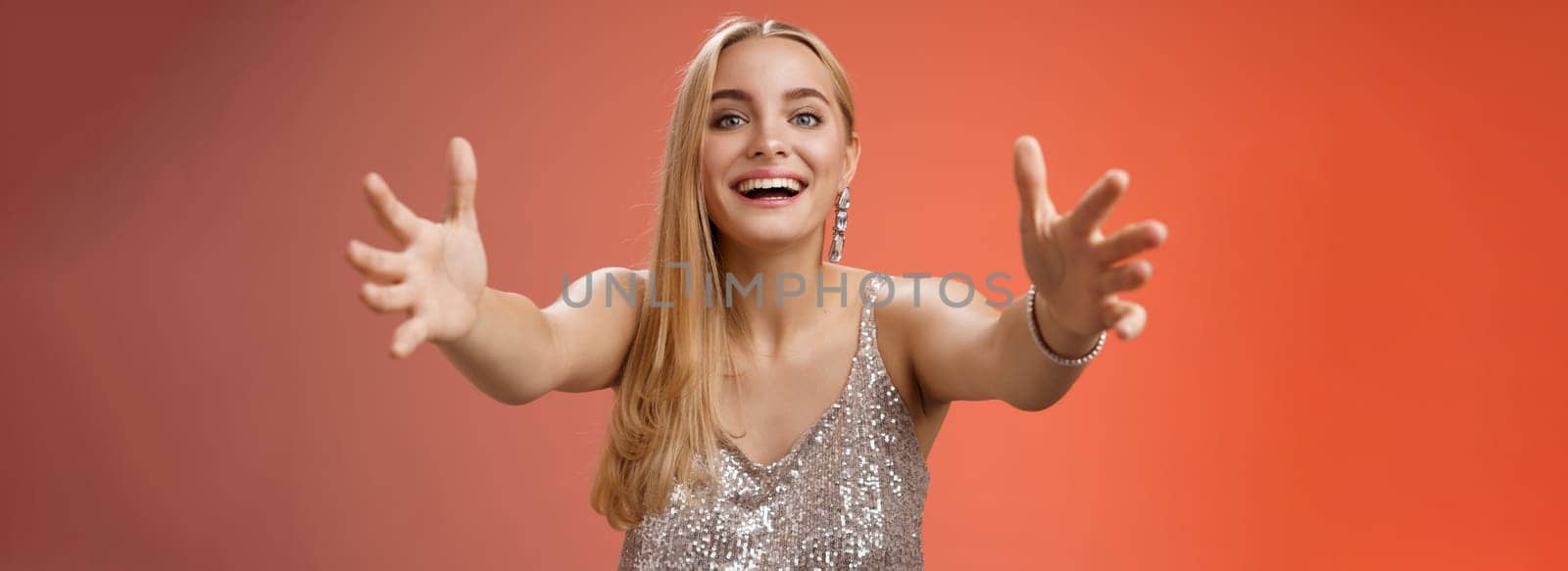 Hospitable charming nice young blond woman wanna hug come closer camera extend arms welcoming embracing cuddling being clingy smiling delighted standing amused red background. Copy space
