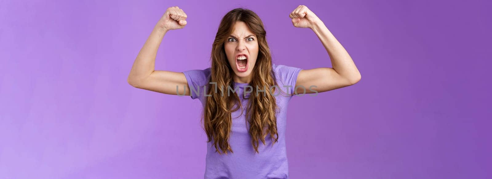 Funny curly-haired girl raising hands fist pump show muscles yelling daring cool shouting encouraged motivated win grimacing strong powerful woman celebrating victory feel like champion. Lifestyle.