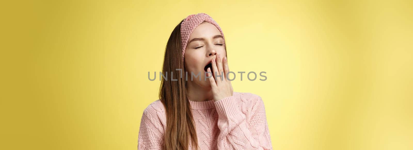 Time to bed. Portrait of tired cute sleepy girlfriend wearing sweater, knitted headband yawning cute with closed eyes opened mouth covered with palm, exhausted, wanting sleep, dreaming fall asleep.