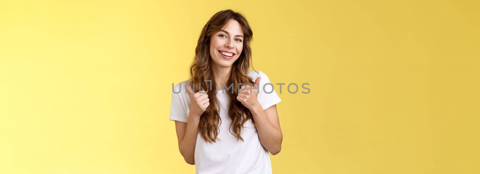 Good have my support. Cheerful positive cute lively curly-haired european girl show thumbs-up approval like gesture tilt head pleased accepting judging fine choice stand yellow background by Benzoix