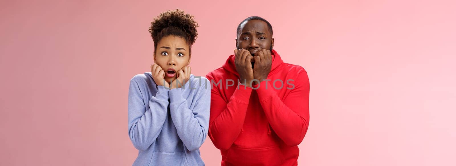 Shocked scared two insecure young african american couple both frightened spiders standing bed terrified freeze from fear holding hands mouth biting fingers shaking horror, pink background.