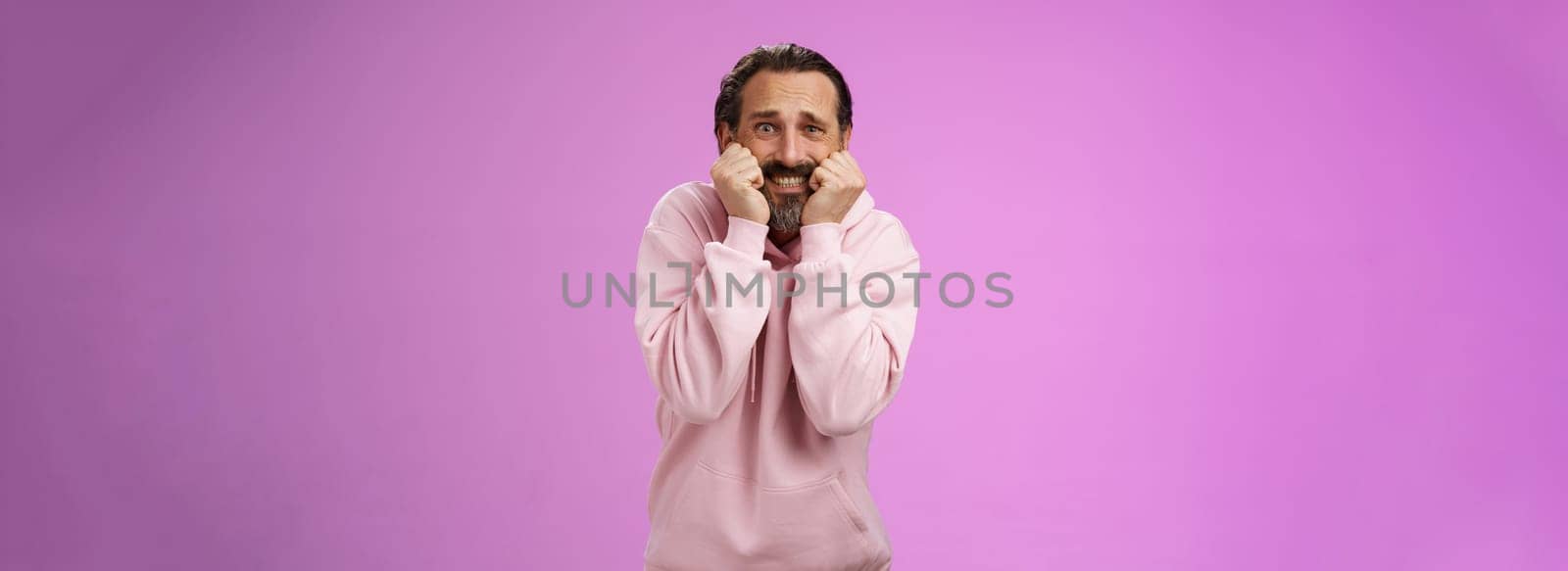 Scared insecure silly adult bearded man grey hair in pink hoodie press palms mouth bite fingers clench teeth shocked frightened widen eyes terrified standing stupor horrified, purple background by Benzoix