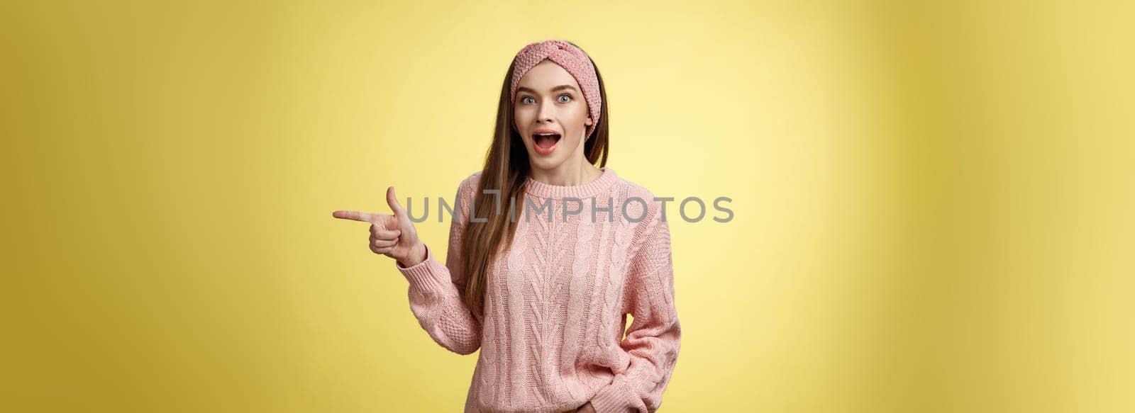 Amused thrilled attractive young female sharing amazement and excitement pointing right dropping jaw seeing unbeliavable awesome product, girl astonished advertising cool promo over yellow background.