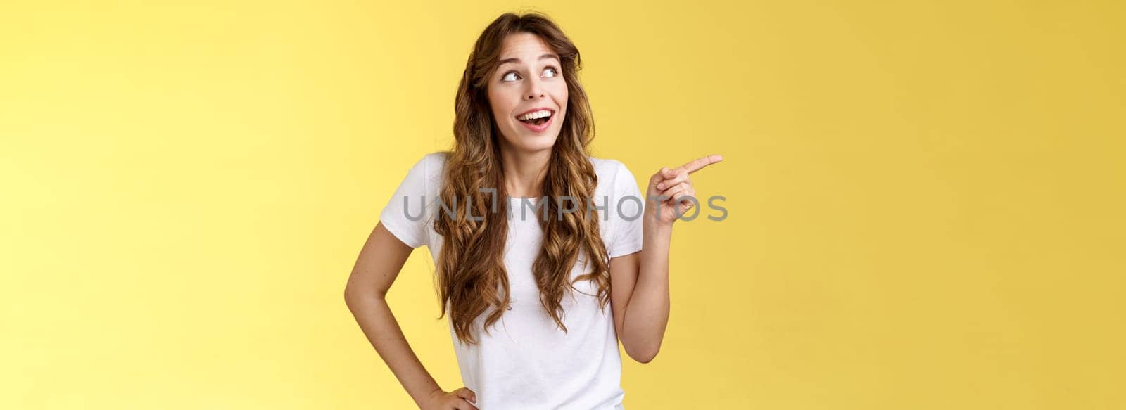 Wondered impressed charismatic fascinated smiling happy girl pointing look upper left corner speechless surprised grinning toothy happiness joy expression contemplate great view yellow background by Benzoix