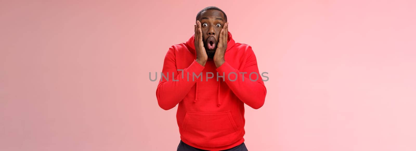 Wow incredible. Portrait impressed surprised african-american bearded guy in red hoodie folding lips bending widen eyes shocked see incredible offer standing amused excited, pink background.