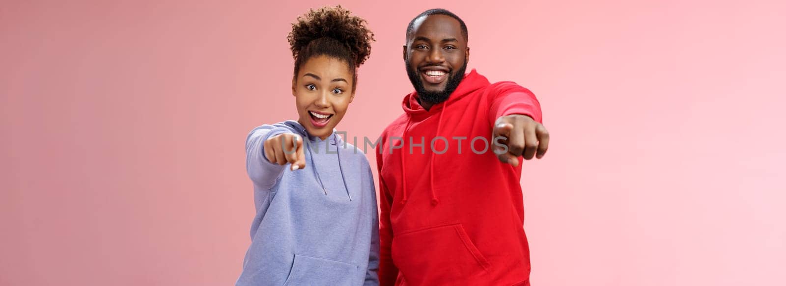 Joyful young attractive happy african-american couple vacation enjoying interesting tour standing impressed amazed pink background pointing index fingers camera awesome curious object by Benzoix