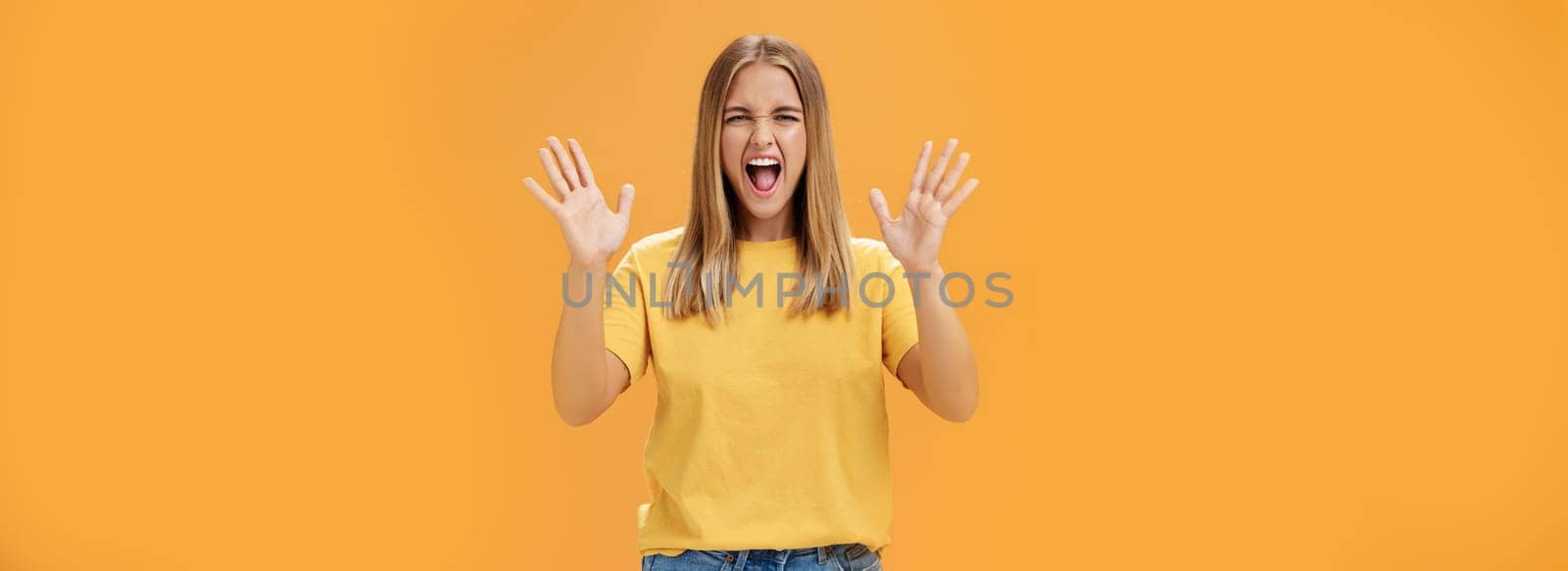 Woman releasing stress yelling with joy and pleasure gesturing with raised arms being daring and rebellious not afraid to show emotions standing passionate and expressive against orange background. Body language concept