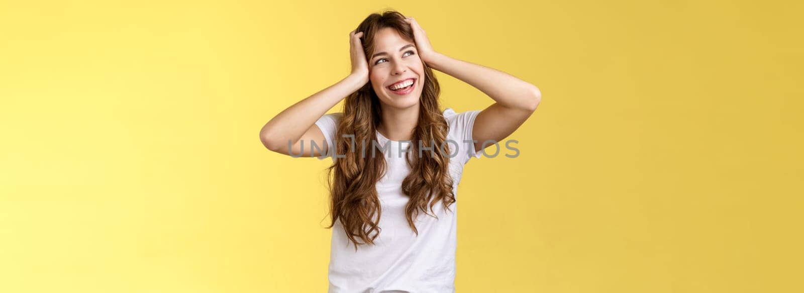 Carefree happy attractive smiling girl hold head curly hairstyle turn away upper left corner sunny summer day excellent lucky weekends standing amused excited adventures start yellow background. Lifestyle.