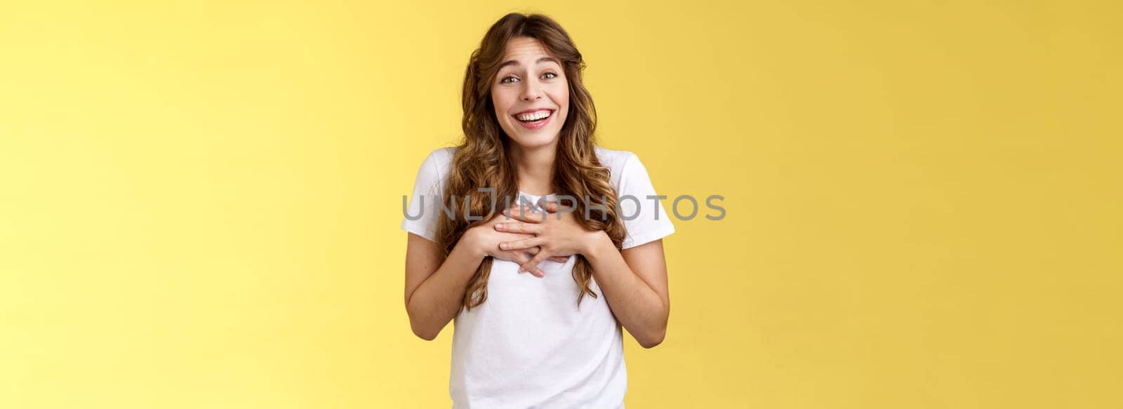Surprised touched grateful charming caucasian curly-haired female appreciate effort thanking awesome gift press hands heart moved lovely nice present smiling broadly thankful yellow background by Benzoix
