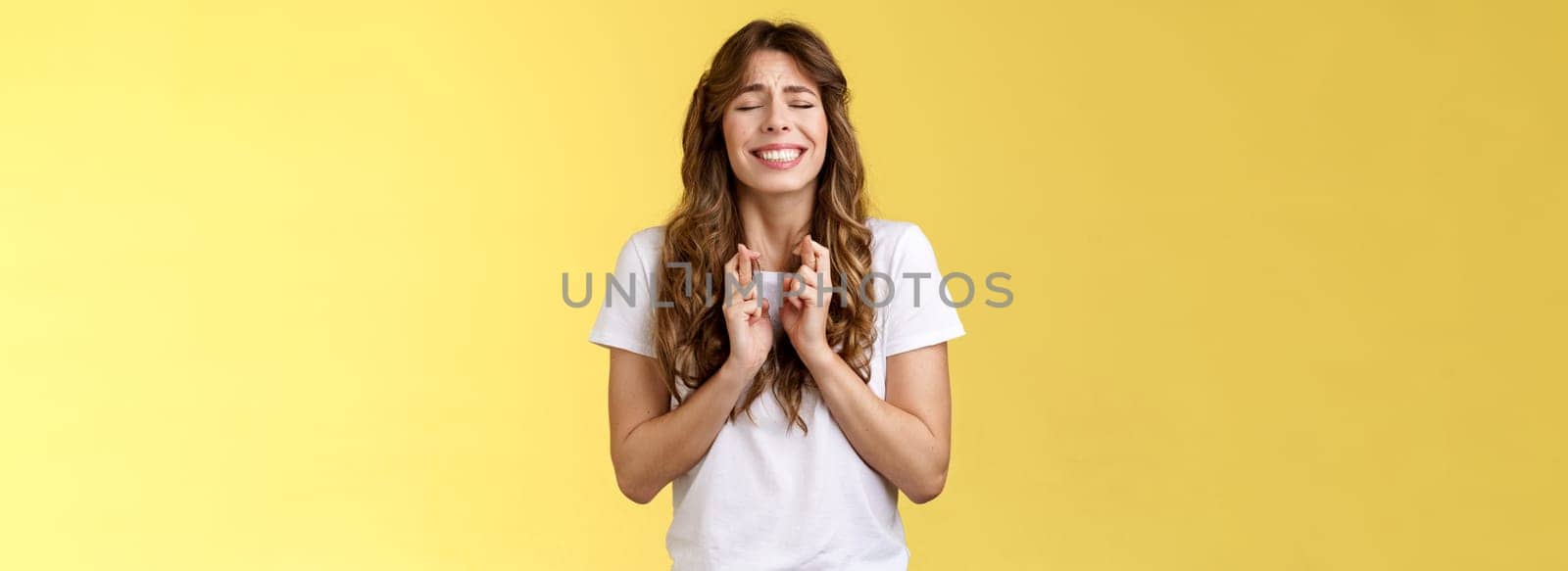 Wishes do come true if believe. Intense nervous cute hopeful pretty girl curly hairstyle close eyes clench teeth smiling hoping good news cross fingers good luck praying dream fulfill.
