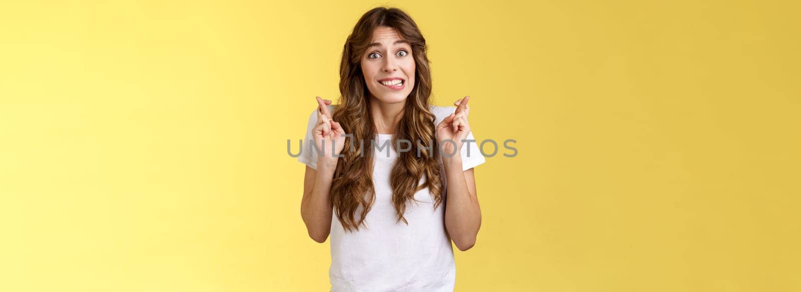 Excited worried cute silly girlfriend anticipating important results nervously biting lower lip unconfidently cross fingers good luck smiling hope dream come true making wish yellow background by Benzoix