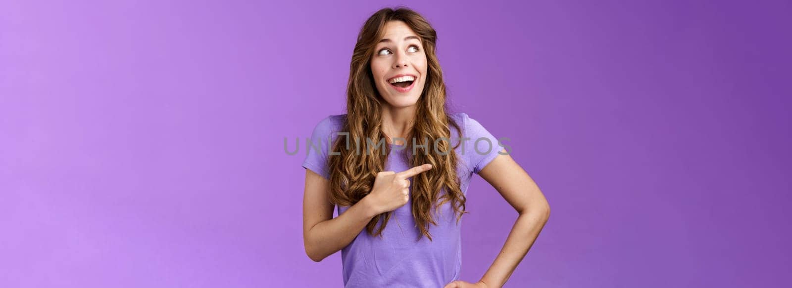 Dreamy wondered impressed cute lively excited positive girl feel happy travel abroad explore new city tourist trip smiling broadly contemplate awesome view look pointing left grinning purple wall. Lifestyle.