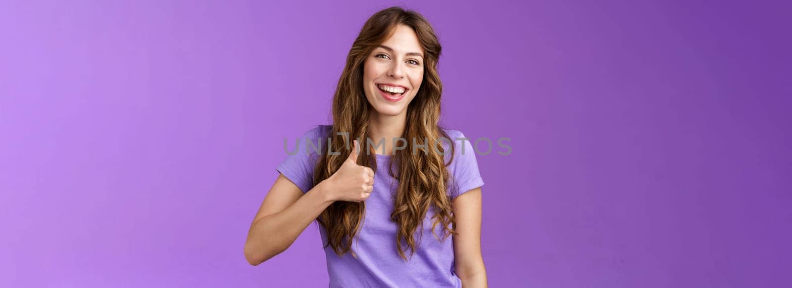 Cheerful supportive lively outgoing caucasian girl like your idea positive opinion give approval show thumbs up satisfied smiling broadly accepting great plan stand purple background.