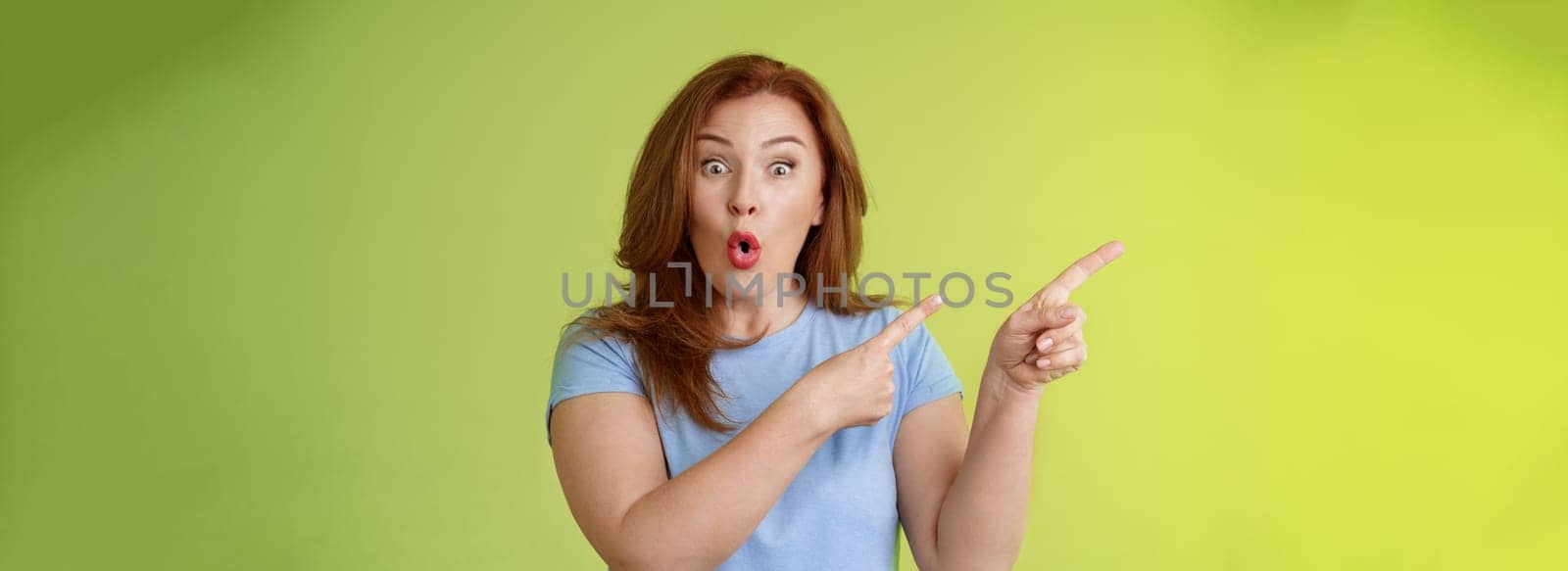 Surprised fascinated enthusiastic redhead middle-aged woman impressed awesome promo fold lips curiousity admiration stare camera thrilled pointing upper left corner great sale advertisement.