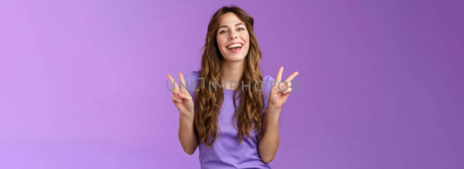 Happy cheerful attractive female express positive upbeat attitude show peace victory signs smiling broadly toothy adorable grin having fun enjoy summer holidays posing photograph purple wall. Lifestyle.