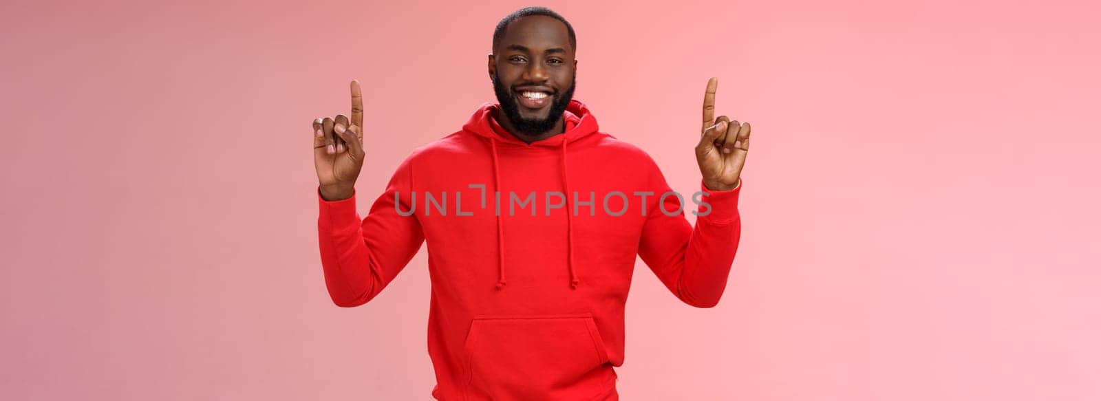 Devious cute african-american bearded guy in red hoodie smiling mysterious know exactly what you want pointing raised index fingers up grinning show perfect copy space promo, pink background.