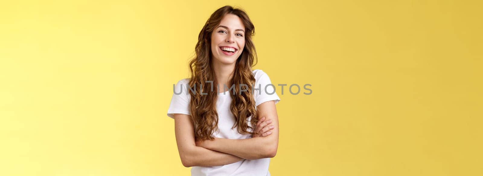 Entertain me. Friendly charismatic female long curly haircut laughing joyfully hang out friends cross arms chest feel chilly slightly cold have amusing pleasant conversation yellow background.