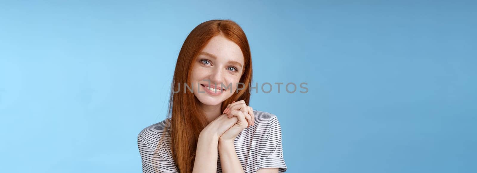 Tender romantic sincere young redhead teenage girl found love look sympathy delight press palms together cute pose smiling happily gazing camera passion lovely grin, blue background by Benzoix