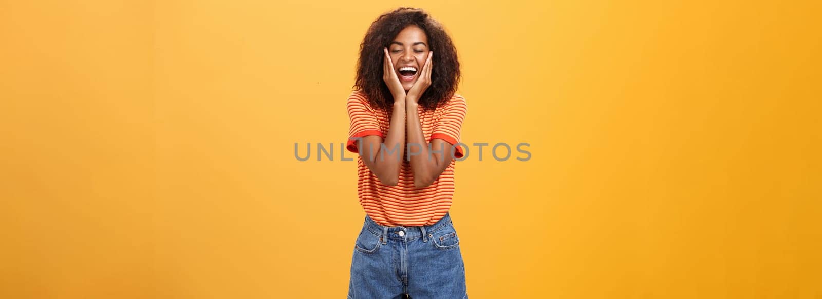 Woman happy and delighted with great result after curing acne with skincare products touching cheeks smiling happily with closed eyes feeling pleased and amused over orange background by Benzoix