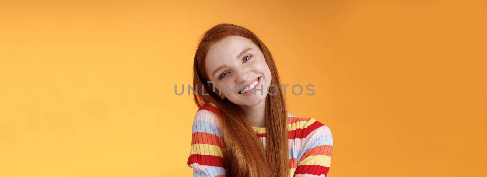 Lifestyle. Tender lively cheerful smiling redhead european girl 20s tilting head leaning shoulder flirting grinning cute make lovely gazes camera coquettish talking boyfriend standing silly orange background.