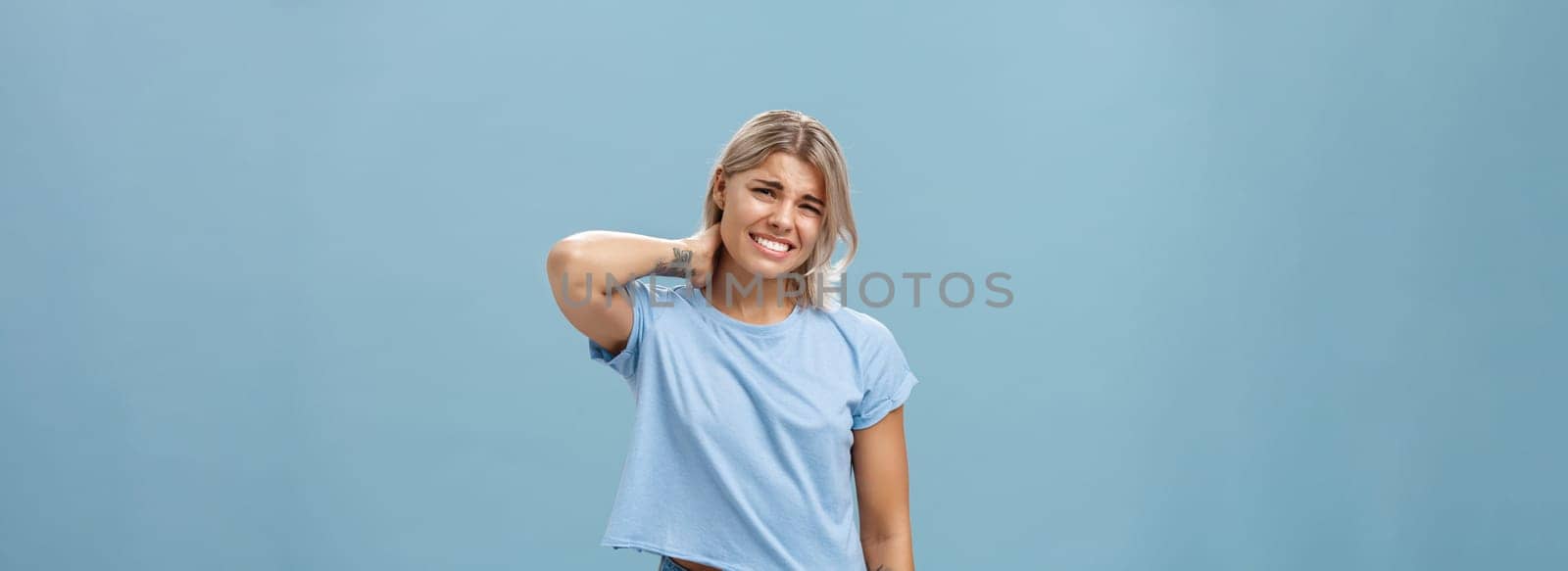 Lifestyle. Girl unwilling to go with friend feeling awkward and unsure how say no frowning and clenching teeth making apologizing face rubbing neck behind saying sorry while rejecting offer over blue background.