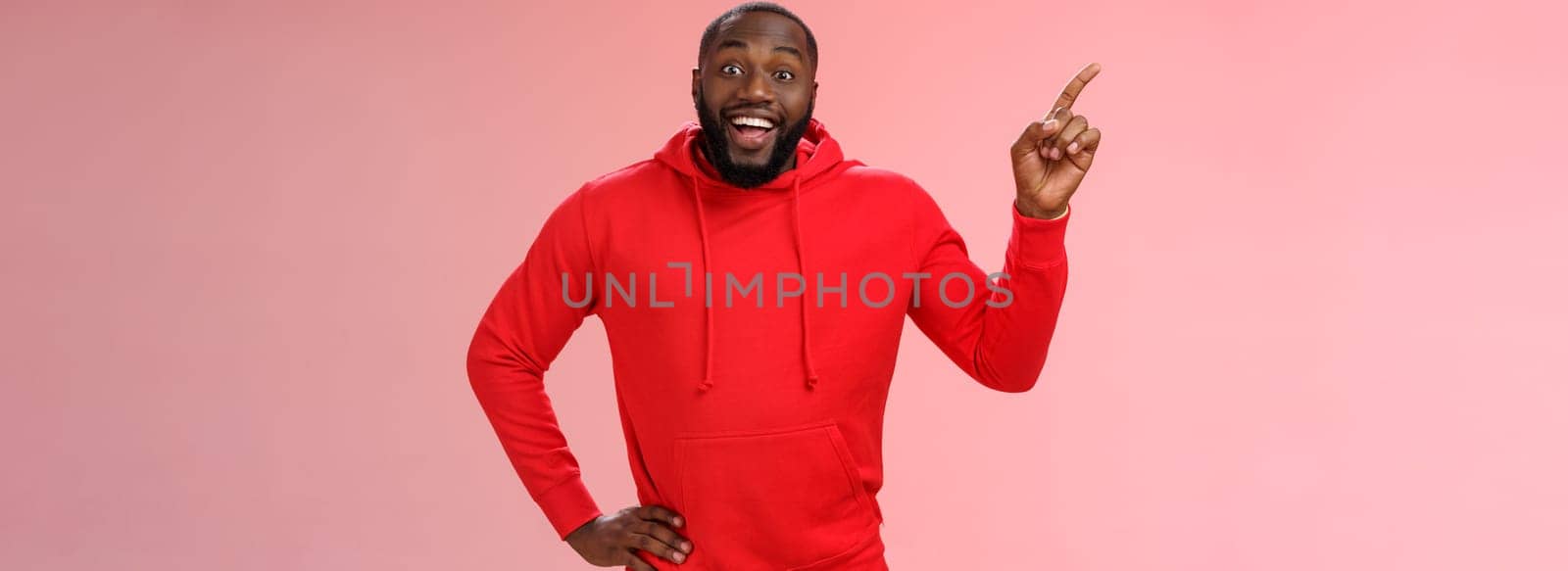 Enthusiastic happy good-looking young black guy beard pointing upper left corner smiling approval like curious about interesting item sale ask question excited impressed, standing pink background.