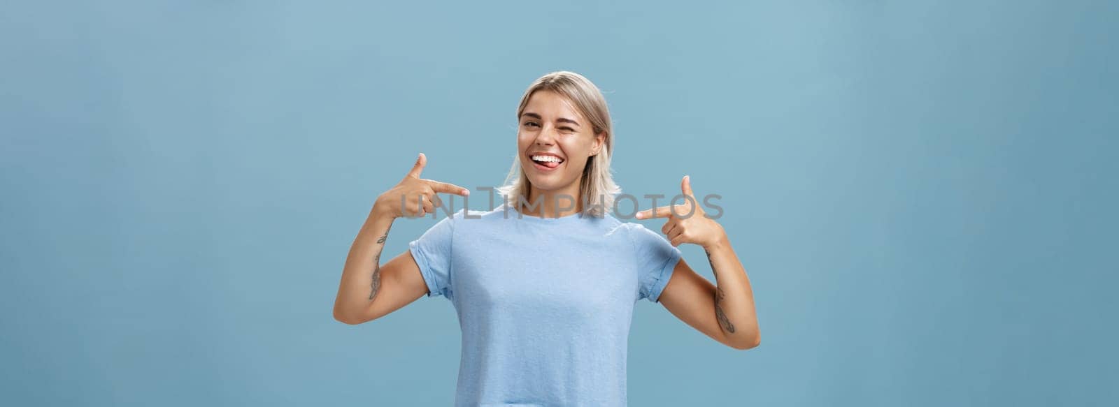 Girl proudly indicates at herself bragging with own achievements. Ambitious creative and smart attractive woman with tanned skin smiling joyfully sticking out tongue and winking pointing at chest.