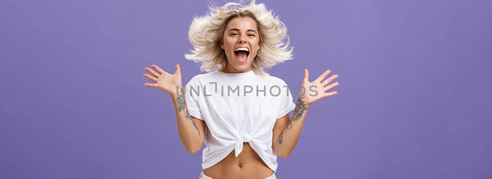 Lifestyle. Studio shot of happy carefree and pleased joyful woman with blonde hair spreading palms aside in delighted pose smiling broadly and gazing entertained at camera jumping while having fun.