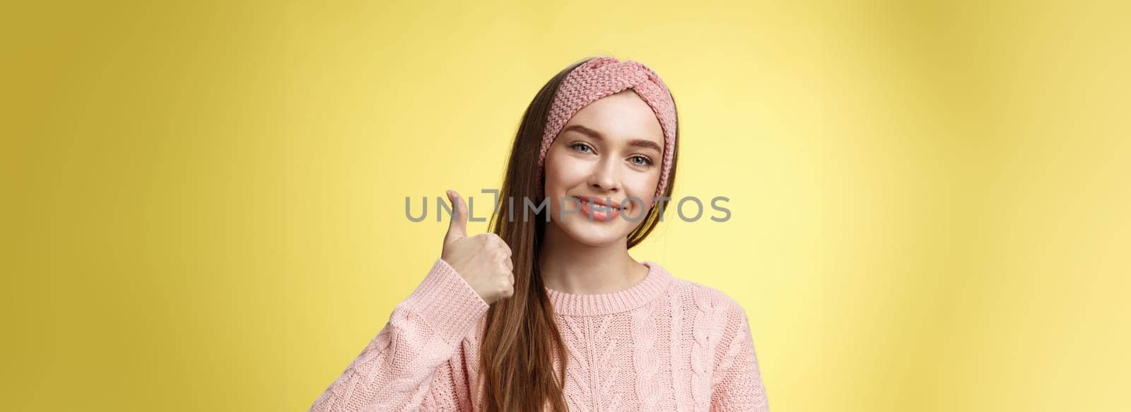 Pretty european young girl in headband, pink sweater smiling delighted, pleased showing thumbs up in agreement, approval, giving good recommendation, liking interesting great idea smiling cheerful.