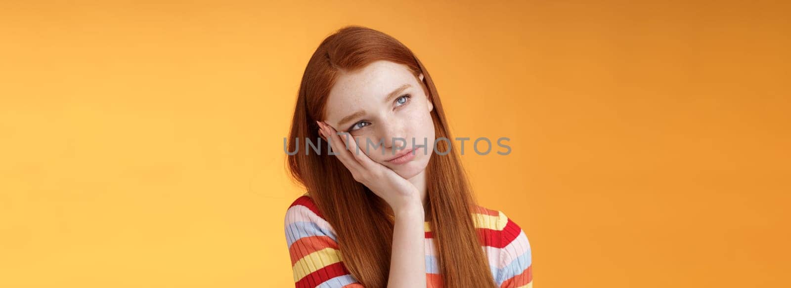 Lonely upset moody cute redhead girlfriend feeling boredom leaning palm look up pouting frowning displeased standing uneasy attend boring meeting, staring uninterested reluctant orange background.