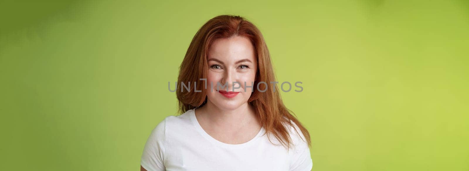 Enthusiastic smiling redhead middle-aged woman grinning joyfully. alluring motivated gaze camera determined reach goal happy watching grandson playing yard pleased have perfect family green background.