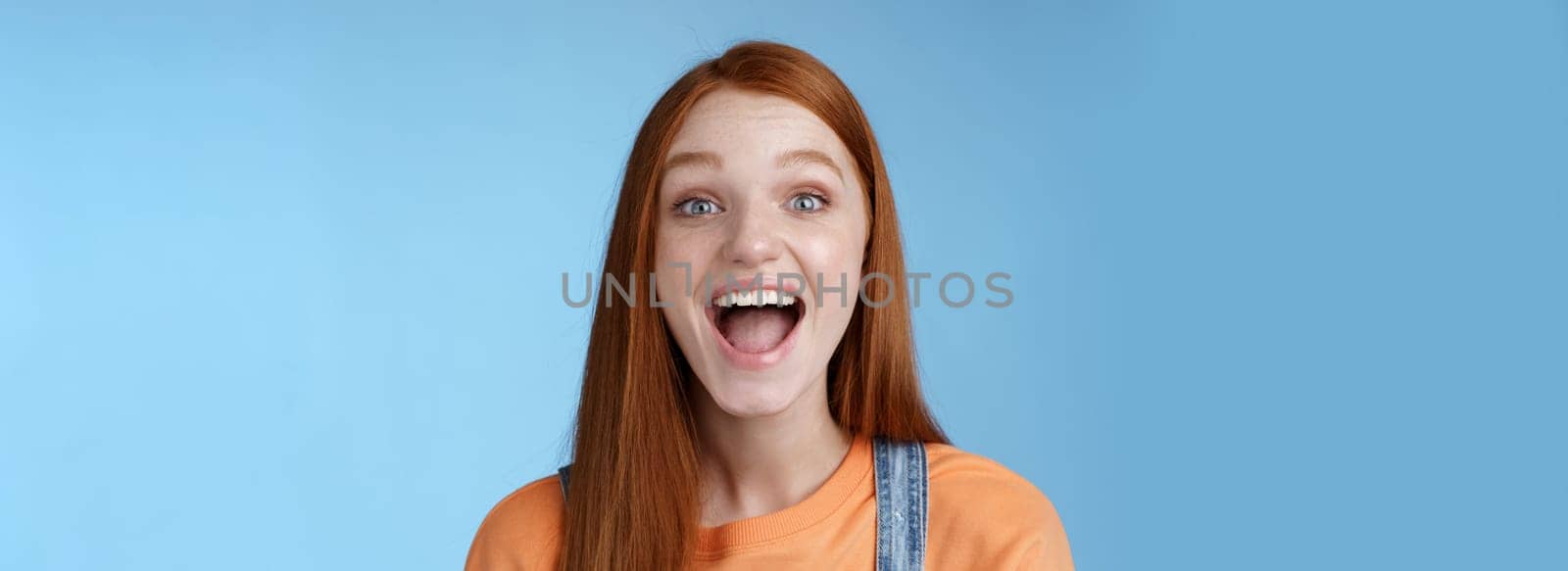 Amused charismatic lively outgoing ginger girl thrilled having fun friends yelling say a showing perfect white smile enjoy friendly joyful atmosphere standing excited positive blue background by Benzoix