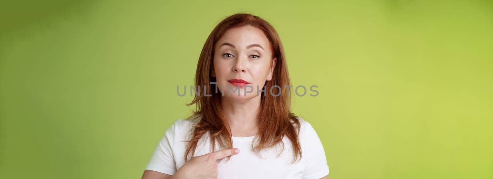 Proud mom pointing herself. Motivated confident redhead assertive middle-aged woman indicating chest volunteering bragging own abilities achievements look camera self-assured green background by Benzoix