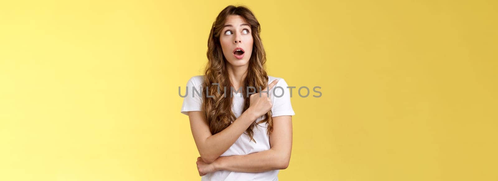 Omg wow no way. Impressed speechless stunned pretty european girl drop jaw astonished open mouth intrigued stare pointing upper left corner admiration surprised glancing curiously yellow background.