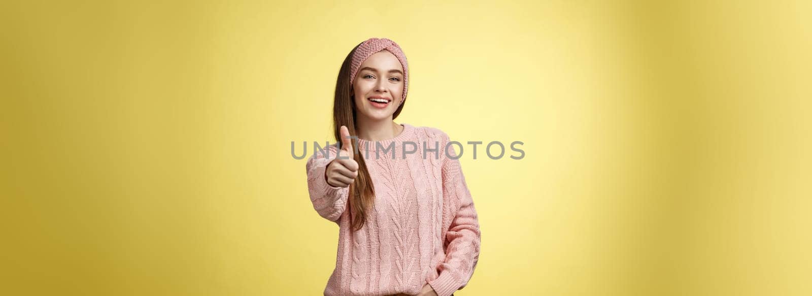 Gestures, emotions and lifestlyle concept. Self-assured positive 20s european woman wearing casual sweater over yellow background showing thumb up gesture, approving, accepting and liking concept.