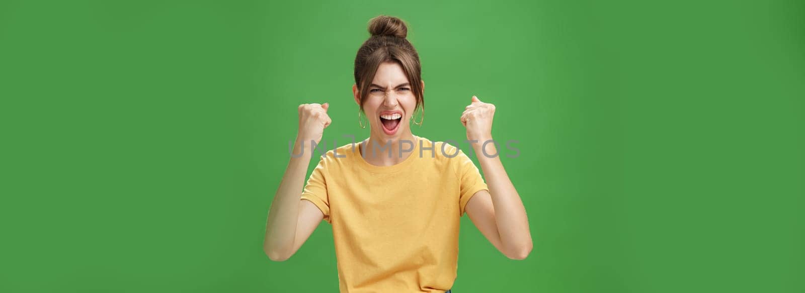 Furious and powerful good-looking emotive woman in yellow t-shirt with gapped teeth yelling in cheer being dedicated fan, supporting favorite team wanting it win raising clenched fists in victory. Copy space