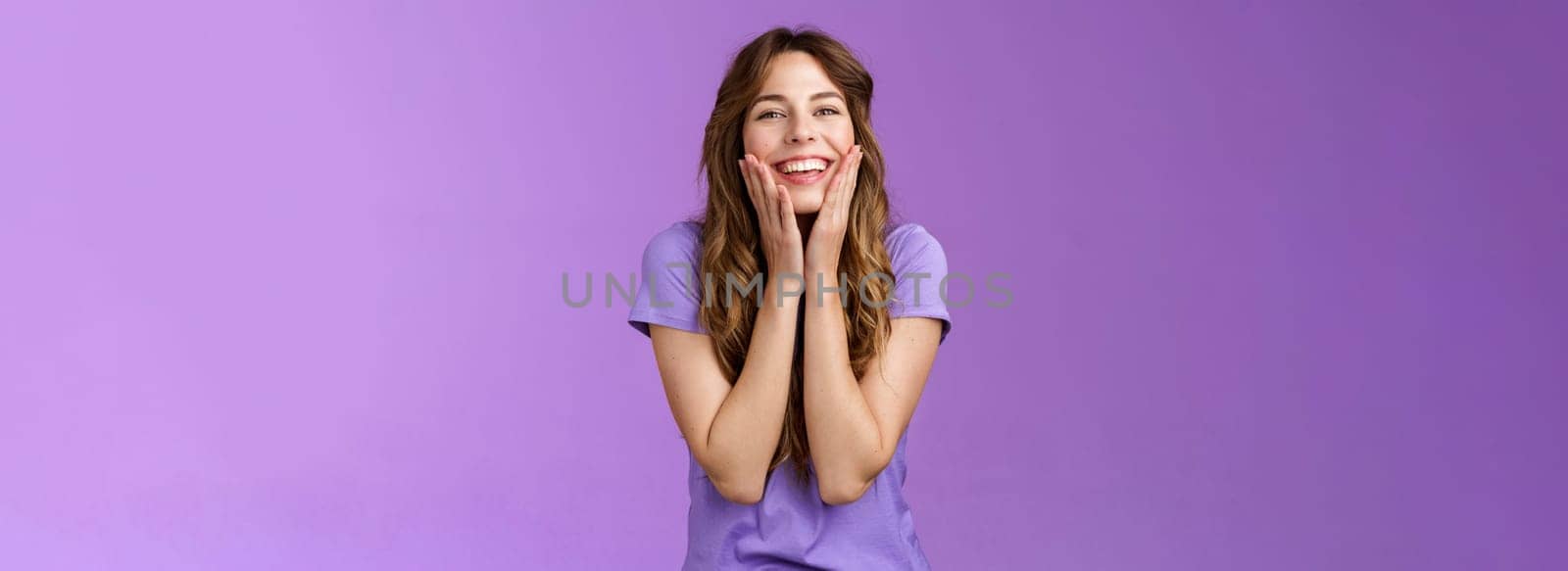 Cheerful lovely cute smiling happy girl grinning delighted touch cheeks having fun enjoy summer warm days look happily express positivity friendship stand purple background. Copy space