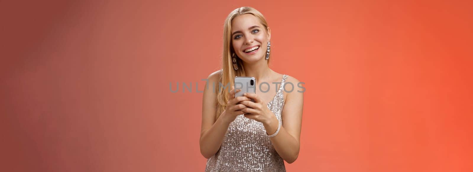 Charming elegant young 25s woman in silver dress brilliant accessorize holding smartphone messaging using app order taxi after nightclub friends party standing carefree smiling camera joyfully by Benzoix