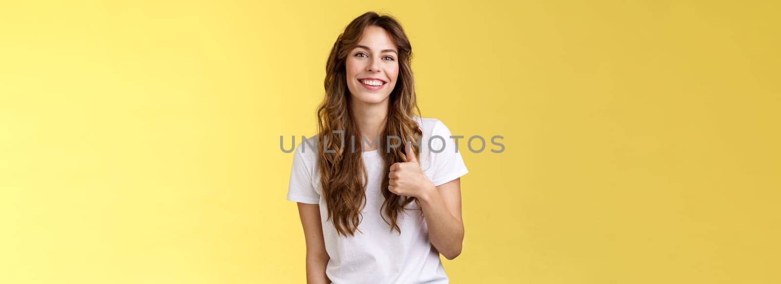 Girl thinks you done great job. Smiling cheerful good-looking woman long curly haircut approve perfect choice give thumb up agree like your style grinning support excellent idea yellow background.
