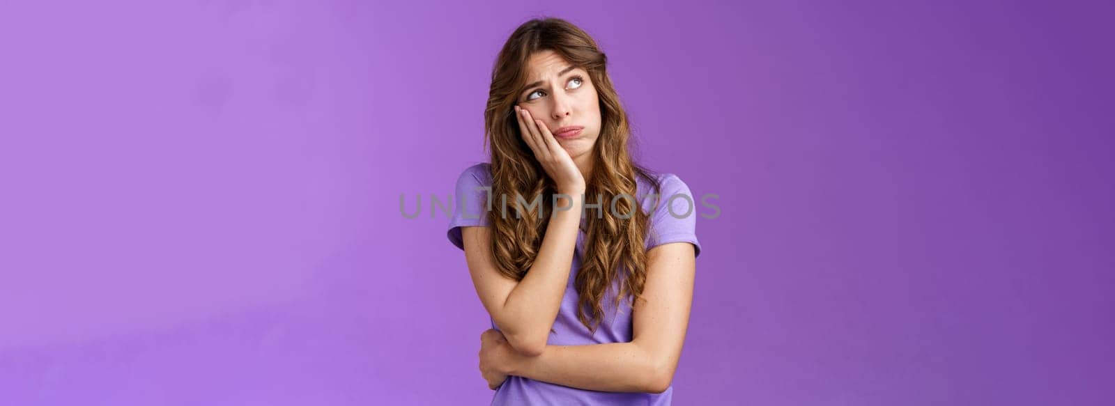 Troubled bored sad european girl long curly brown hair lean palm look up indifferent sighing lonely dying boredom home alone nothing do thinking regret missed party stand purple background. Lifestyle.