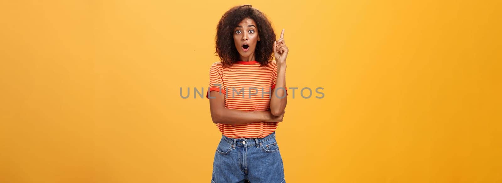 Girl finally understood riddle adding suggestion outloud. Excited thrilled good-looking dark-skinned woman staring amazed raising index finger in eureka gesture having idea over orange wall by Benzoix