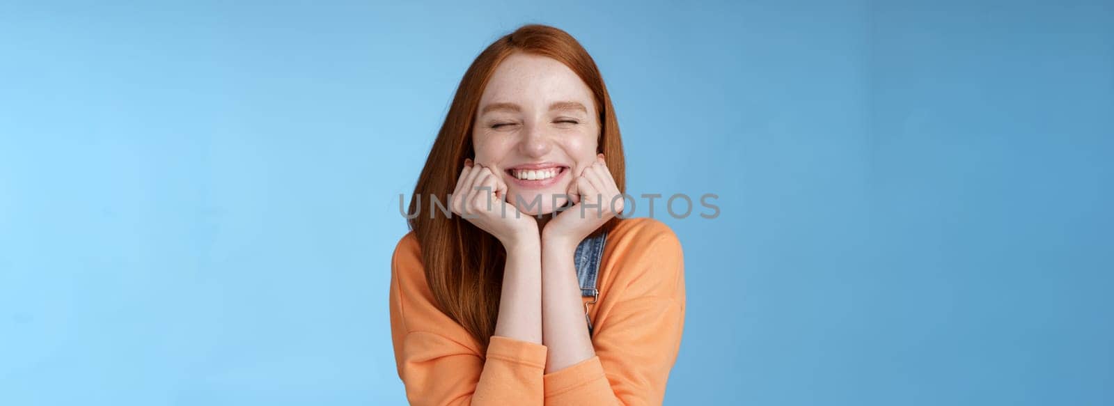 Lifestyle. Silly cute happy redhead girlfriend smiling broadly close eyes dreamy squeez cheeks delighted asked date guy likes standing blue background rejoicing have fantastic lucky day triumphing.