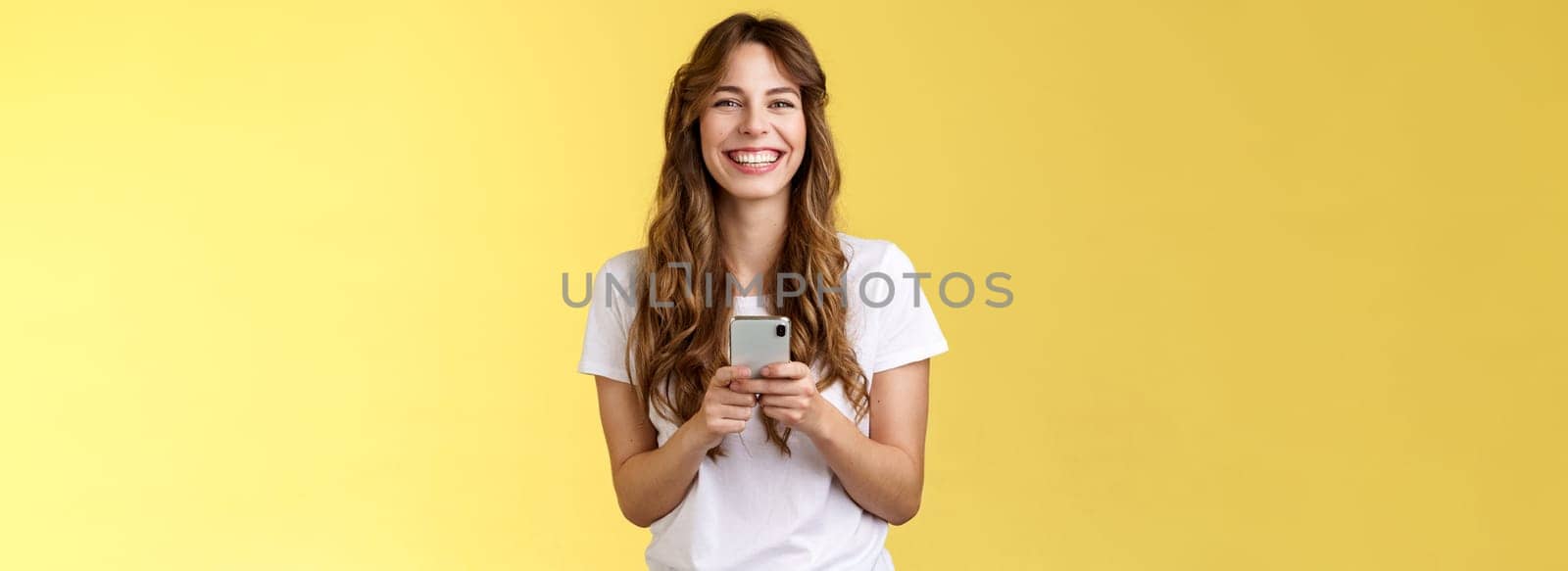 Cheerful carefree happy lively girl hold smartphone using awesome funny app playing cool game relaxing waiting friend park browsing social media using mobile phone look camera upbeat smiling by Benzoix