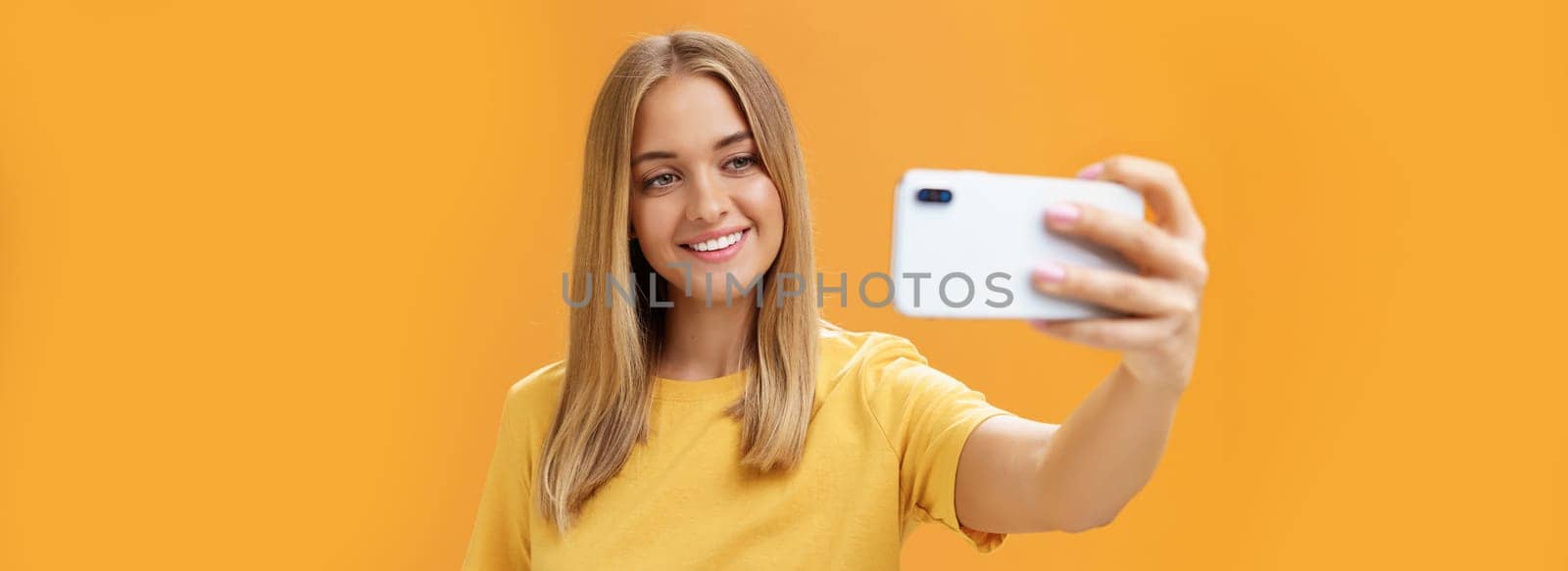 Waist-up shto of outgoing and charismatic pretty confident woman with no makeup and tanned skin holding smartphone pulled on distance smiling broadly at cellphone screen while taking selfie. Technology concept