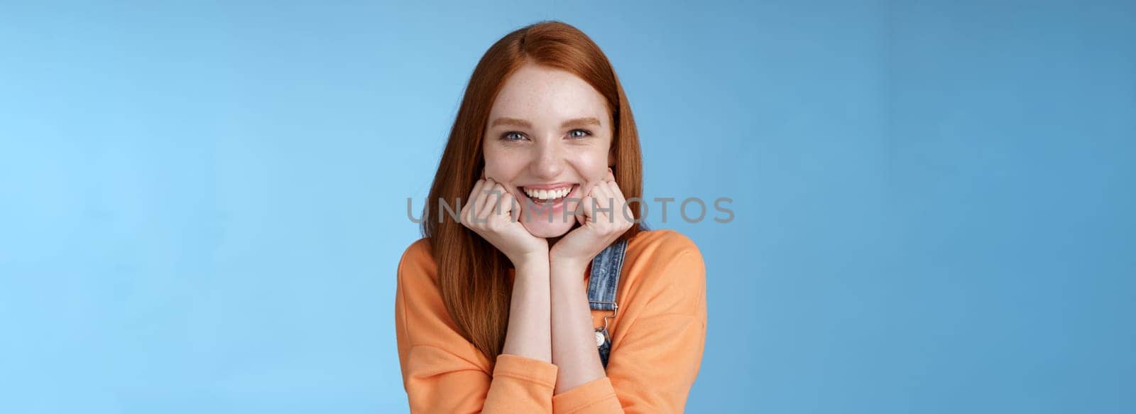 Enthusiastic sassy good-looking redhead caucasian girl lean head palms look amused intrigued listen interesting story pleased smiling laughing silly jokes standing blue background excited happy by Benzoix