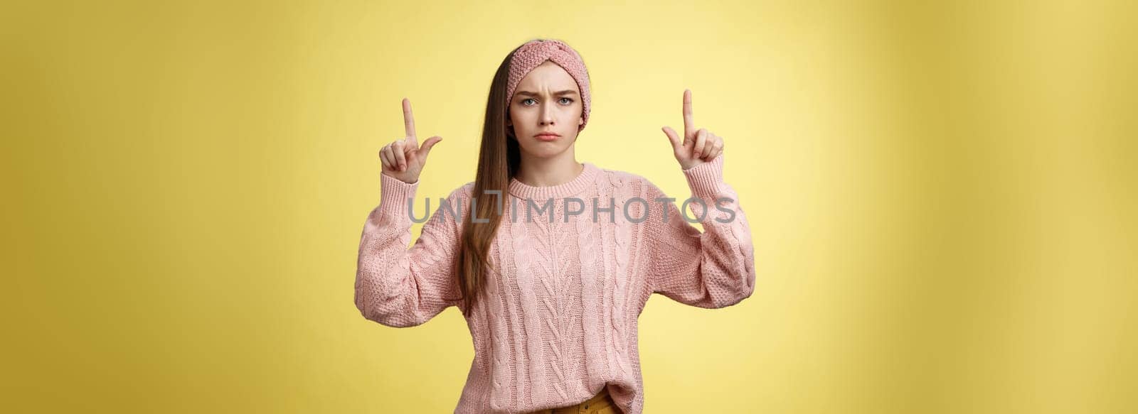 Moody disappointed and upset unamused cute young european girl in knitted warm sweater headband expressing dislike and disagreement pointing up, sulking frowning displeased unhappy with bad choice by Benzoix