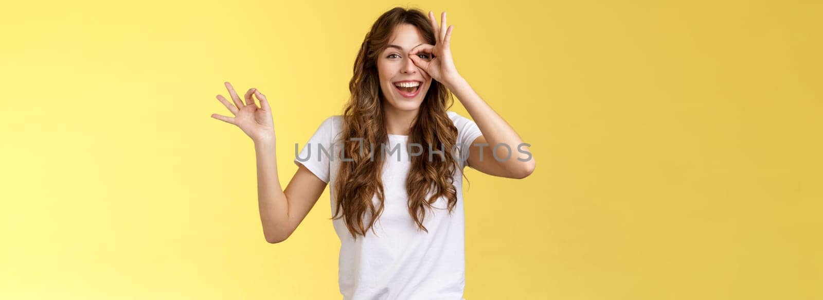 Friendly charismatic enthusiastic happy woman having perfect day show okay ok circle gesture look through ring amused wondered smiling broadly delighted express joy admiration yellow background by Benzoix