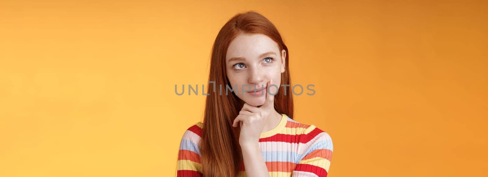 Creative thoughtful young smart redhead female student thinking ideas project look upper left corner dreamy touching lip pondering choice, taking important decision what order, orange background.